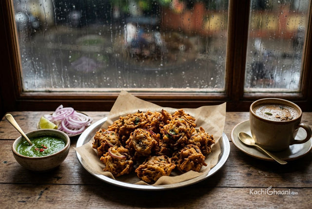 Crispy onion bhajiya on a steel plate with green chutney and a cup of chai by a rainy window