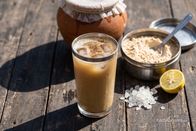 Meetha Sattu ka Sharbat, a tall steel-rimmed glass of meetha sattu sharbat on a dark weathered wooden table