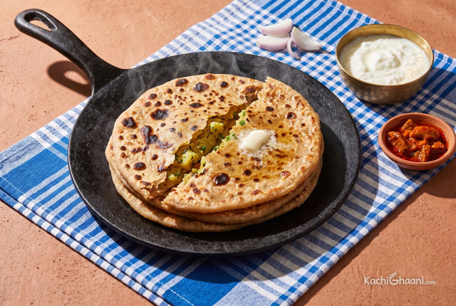 Stack of golden aloo parathas torn open, melting butter on top, curd and pickle beside