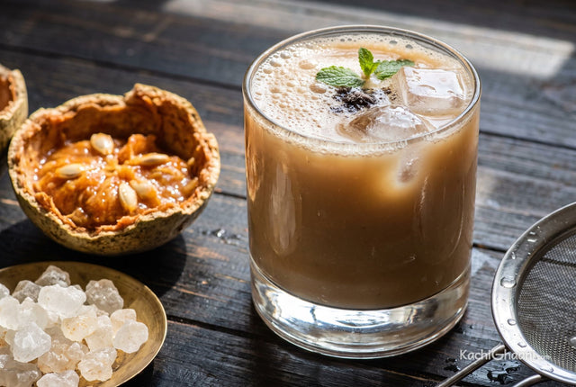 Bel ka Sharbat, a heavy glass tumbler of bel sharbat on a dark weathered wooden table