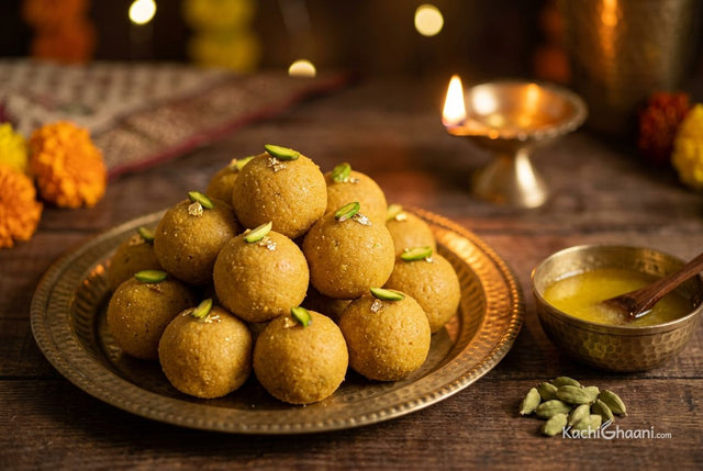 Besan laddoo topped with pistachio on a brass plate, with a lit diya behind