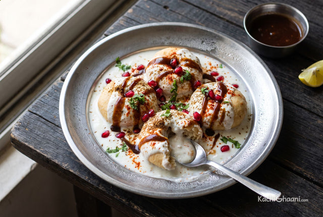 Dahi Vada, plump pale golden urad dal vadas sitting low in thick chilled white curd on a wide steel plate