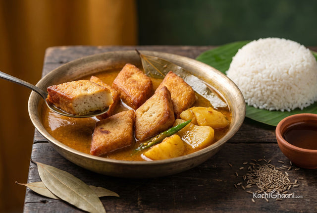 Dhokar Dalna, six golden-brown diamond-shaped chana dal cakes half submerged in a glossy orange-brown gravy