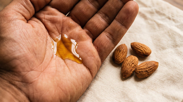 Thick golden almond oil resting in a cupped palm with whole raw almonds on a cotton cloth nearby.