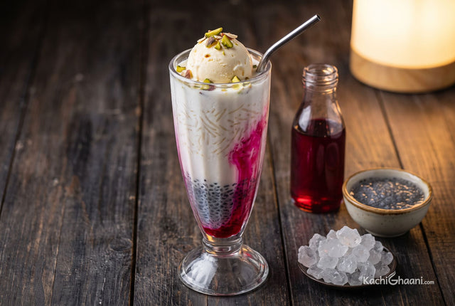 Rose Falooda, a tall clear footed glass of rose falooda on dark weathered wood