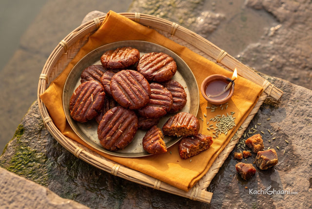 Deep brown ridged thekua piled on a brass plate beside a clay diya
