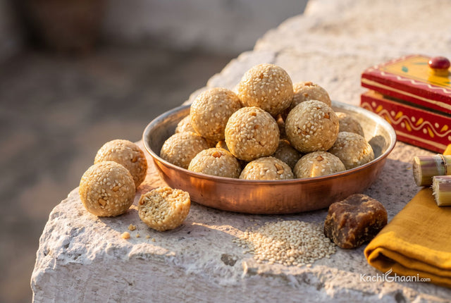 Small sesame and jaggery ladoos piled in a copper bowl, one broken open