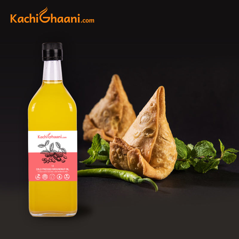 KachiGhaani Truly Cold Pressed Groundnut Oil in a 1 L glass bottle beside freshly fried samosas